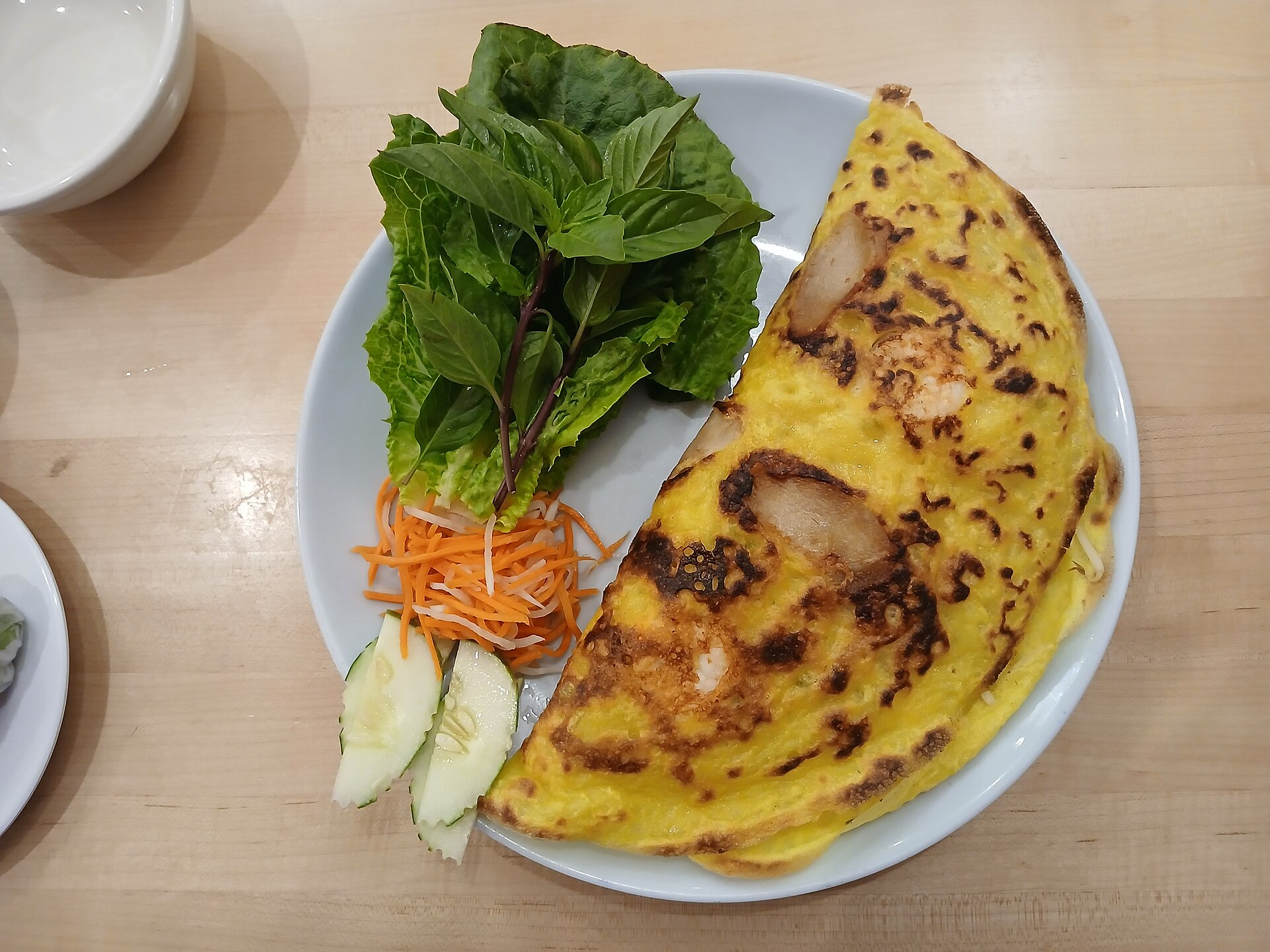 A golden crispy banh xeo crêpe folded over shrimp and pork, served with fresh herbs and dipping sauce