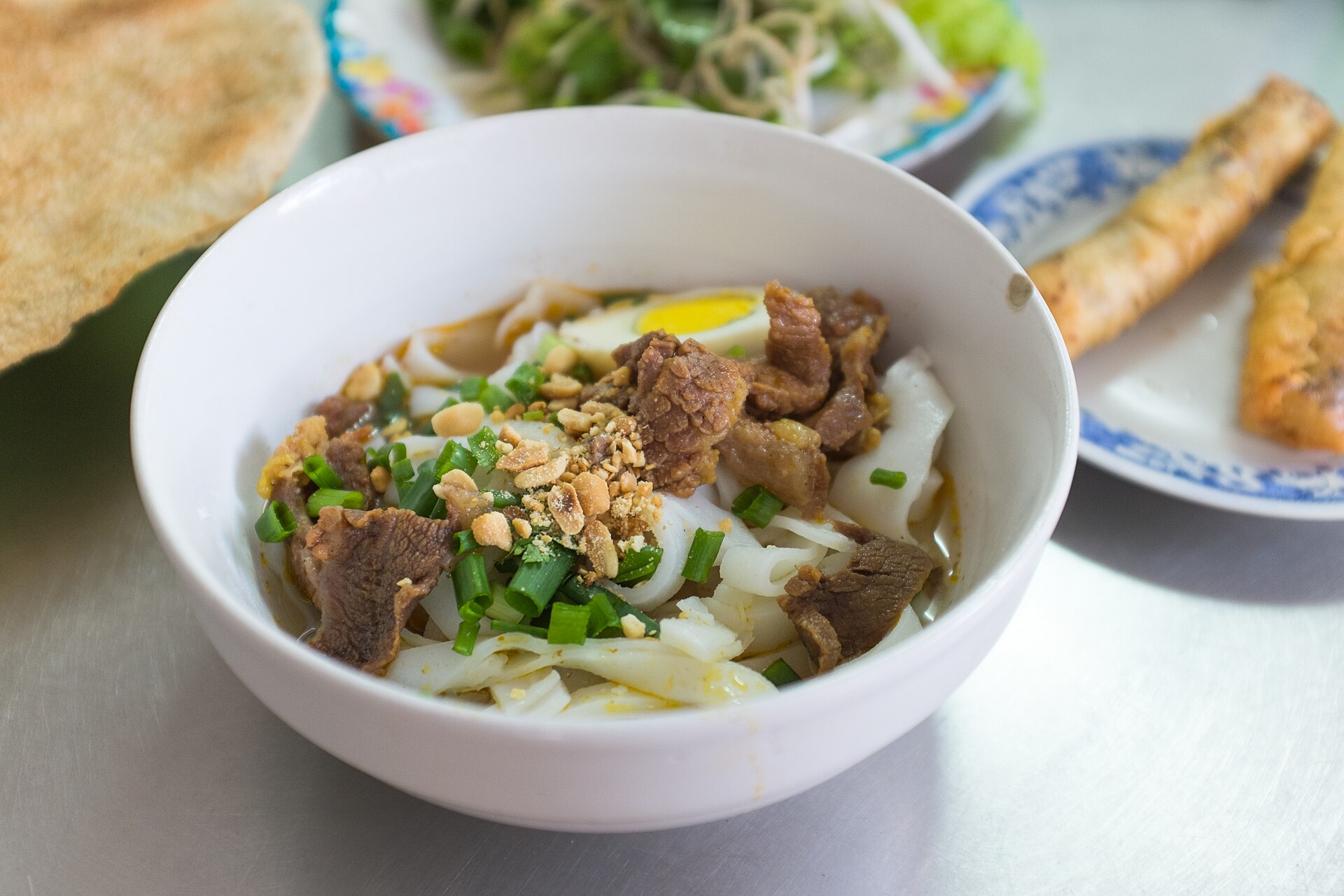A bowl of Mi Quang — wide turmeric-yellow rice noodles topped with shrimp, pork, peanuts and herbs